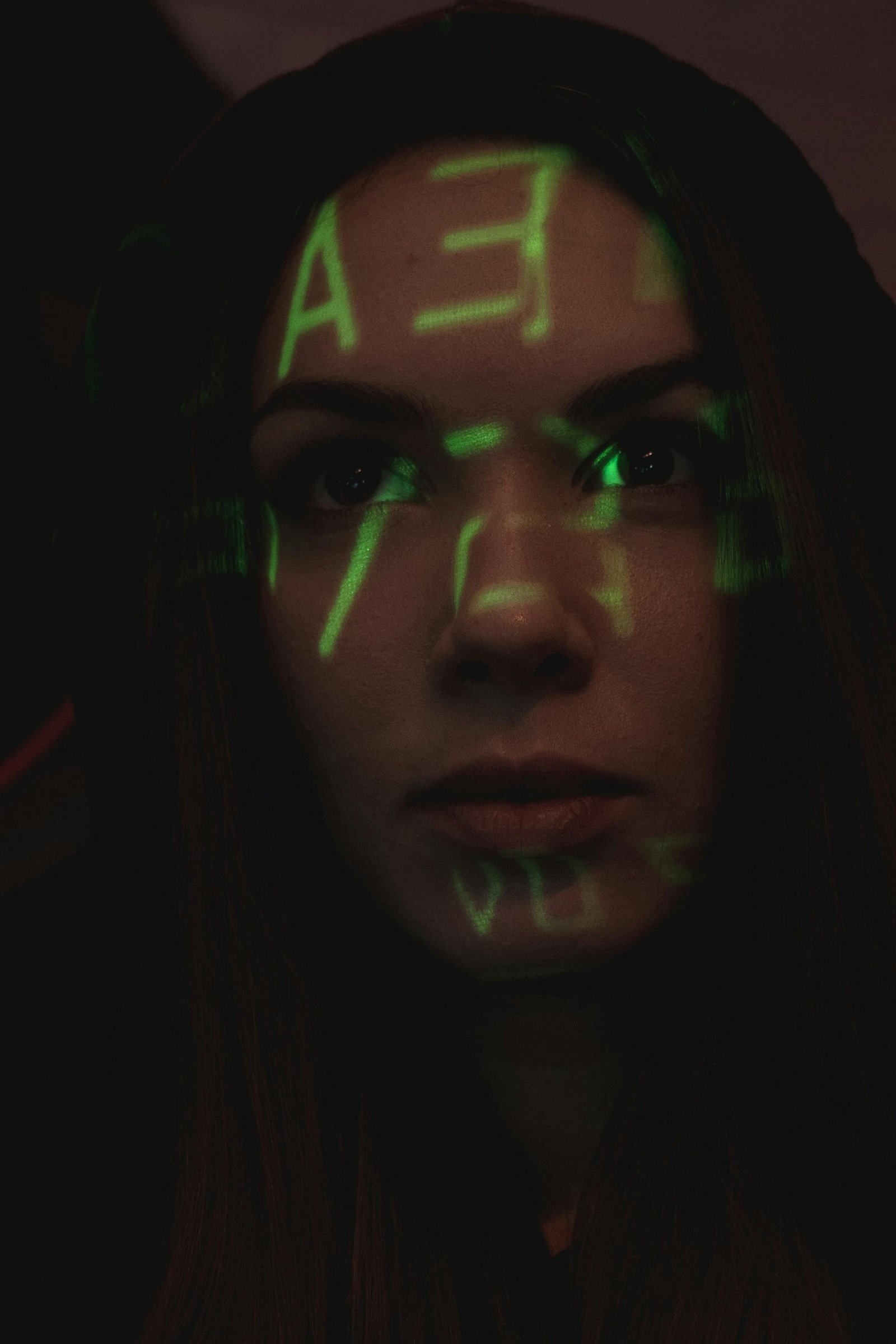 Person's face lit by projected green matrix-style code in a darkened room