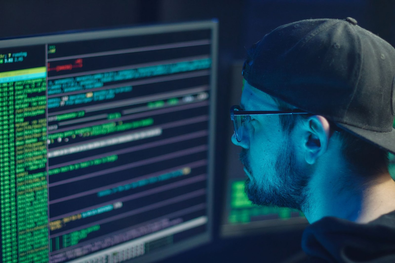 Hooded coder at a monitor filled with code in green text
